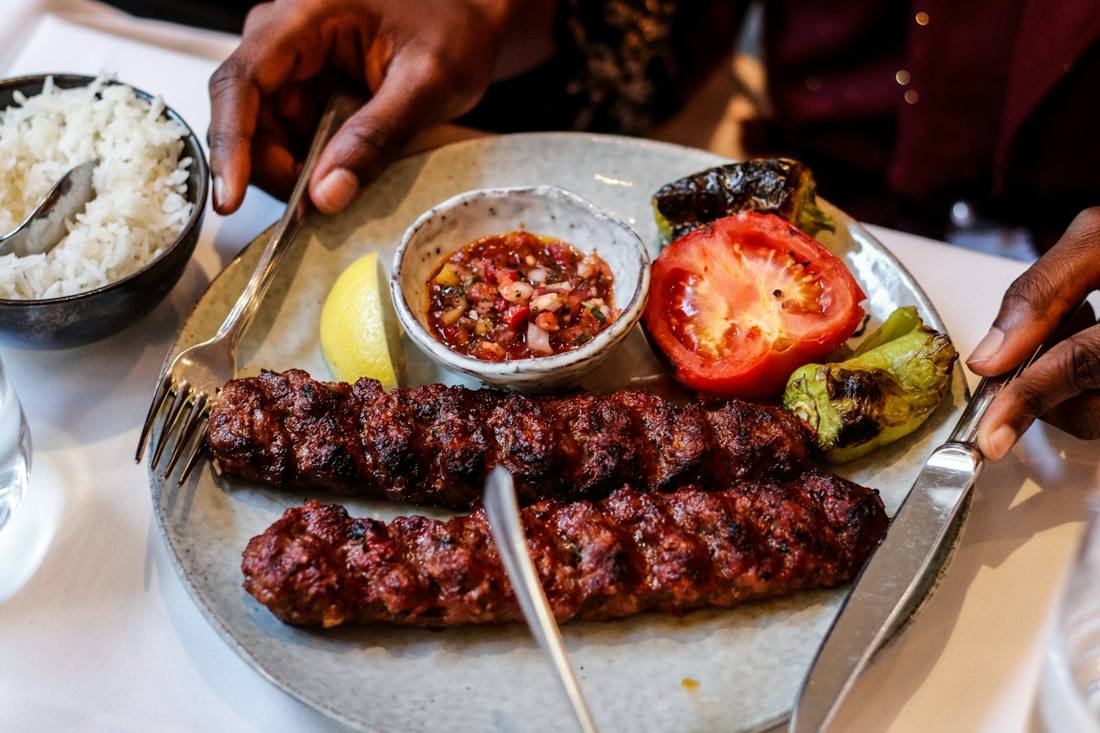 Two Adana kebabs with rice and grilled tomato