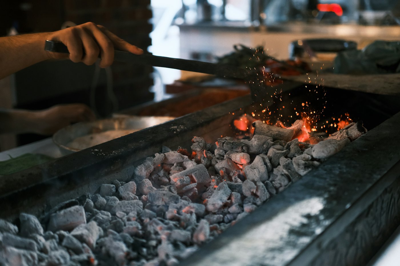 The grill master turning glowing charcoal with tongs